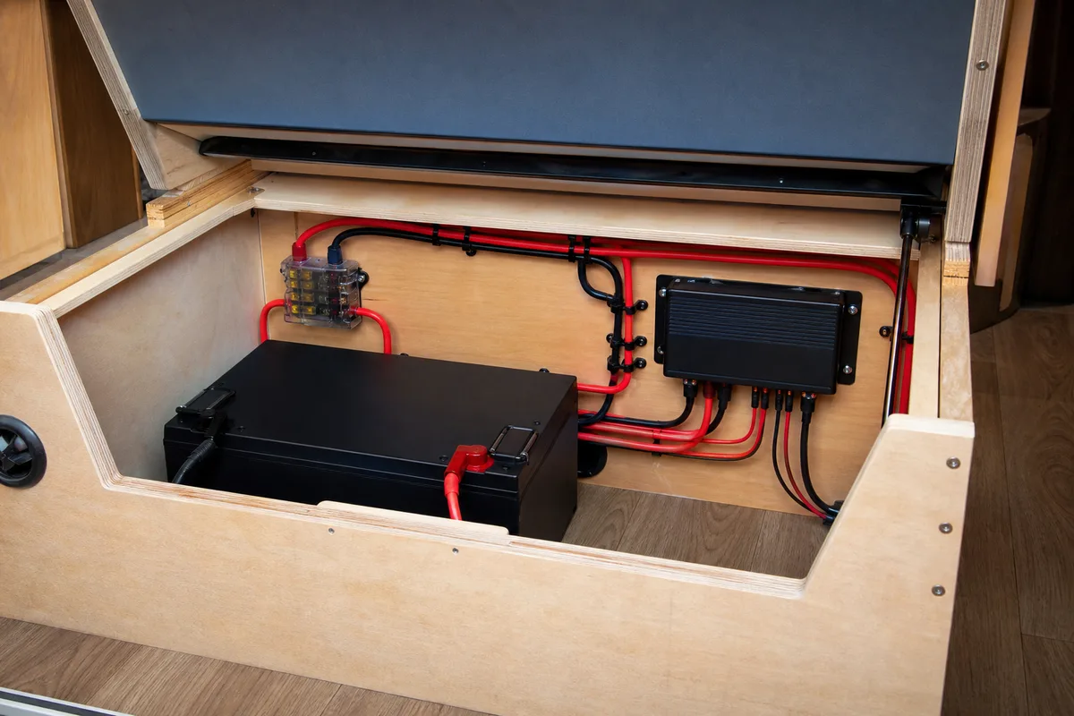 Batterie lithium et régulateur solaire installés dans un coffre technique en bois sous une banquette de van